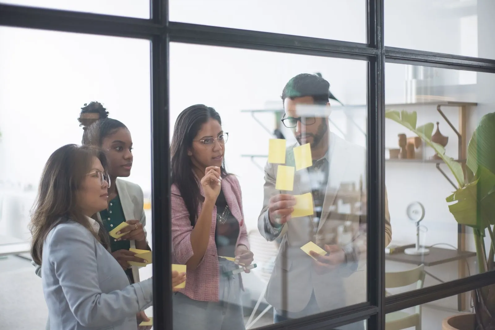 Four colleagues planning a launch with sticky notes on a glass wall