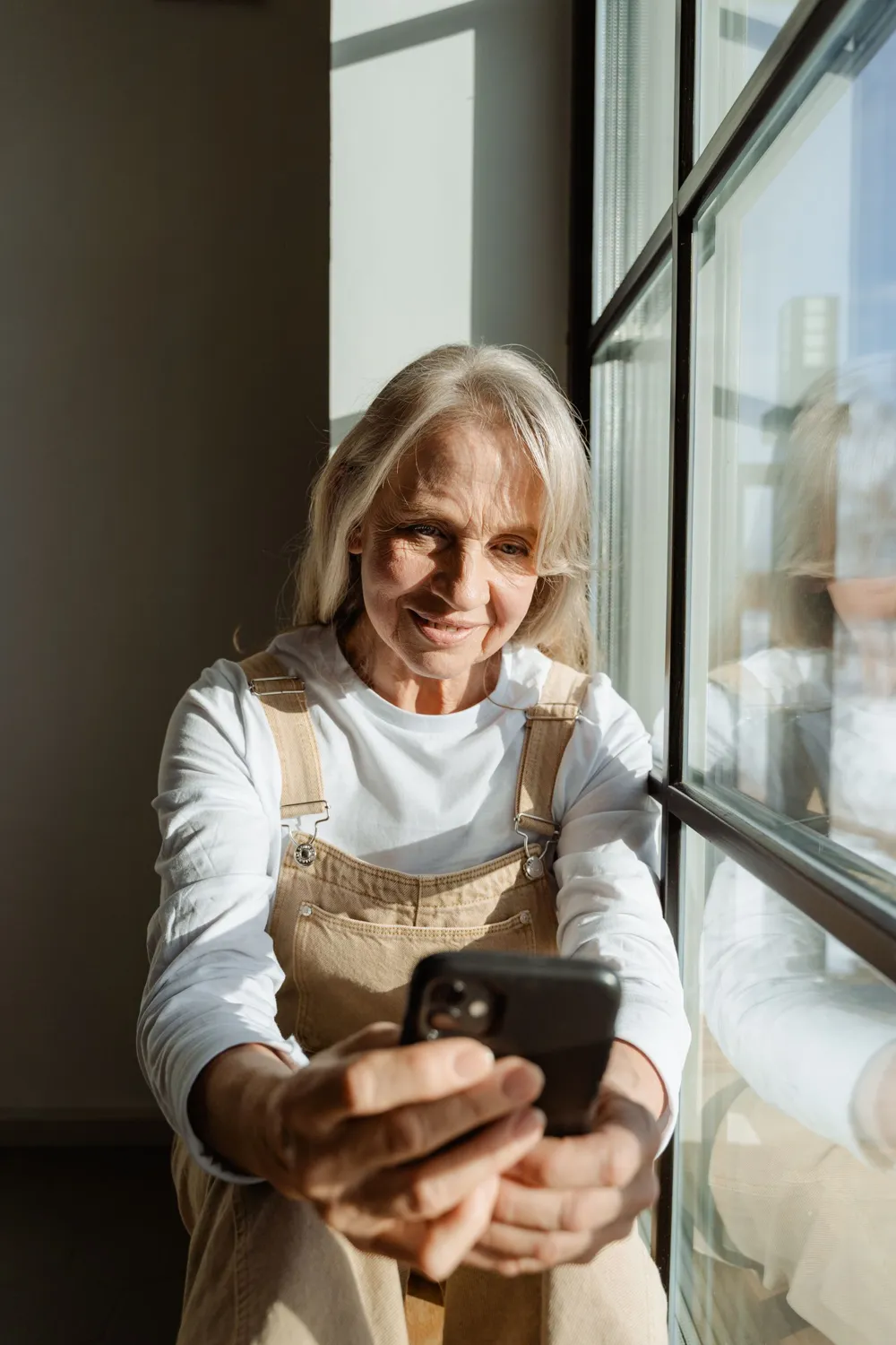 A woman by a sunny window reading something on her phone